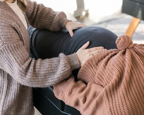 A chiropractor assists a baby lying on a pillow while a young boy watches, smiling.